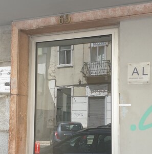 A building entrance with a number '69' above the door, a sign indicating 'AL' (Alojamento local), and a parked car in front.