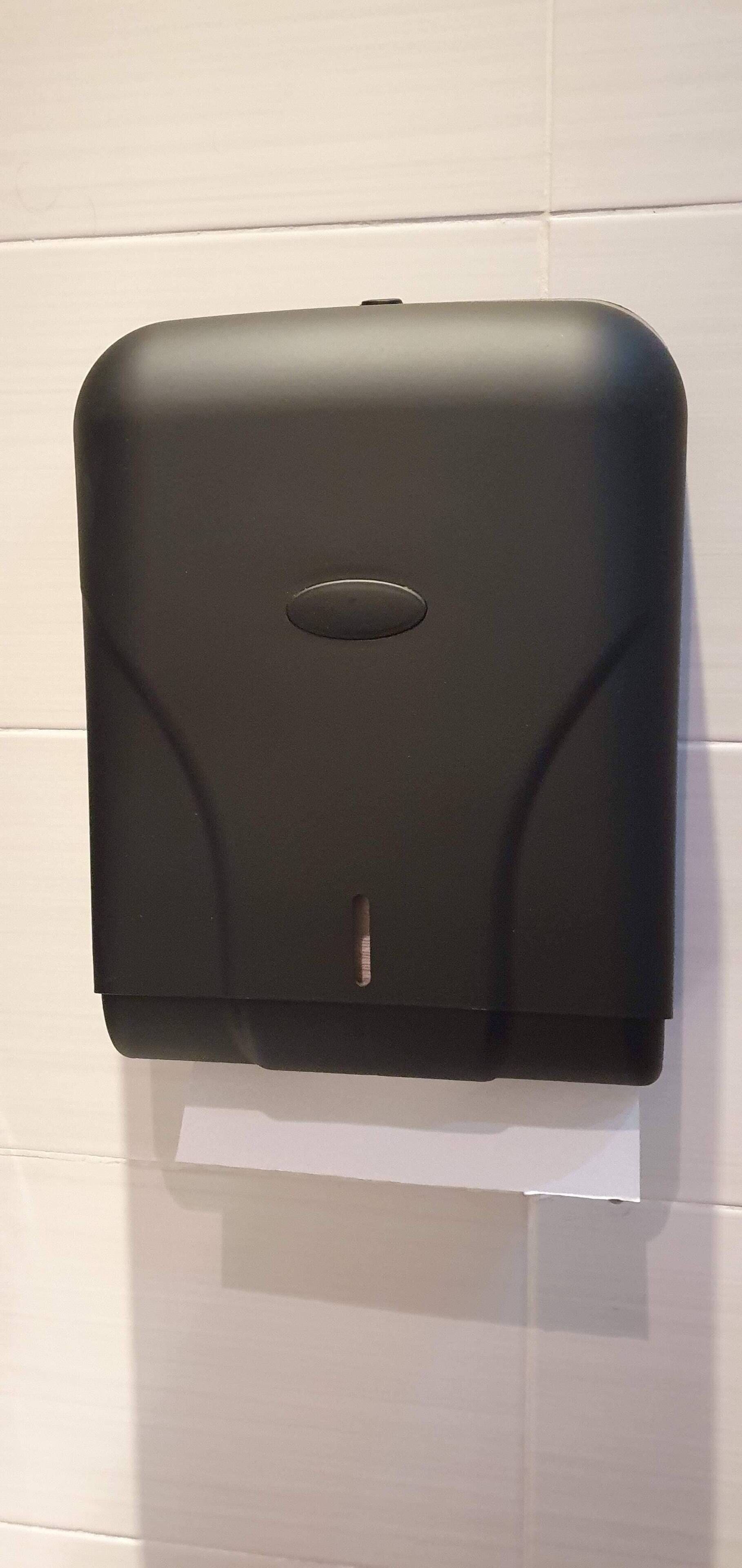Un erogatore di gel disinfettante nero fissato a una parete rivestita di piastrelle bianche.