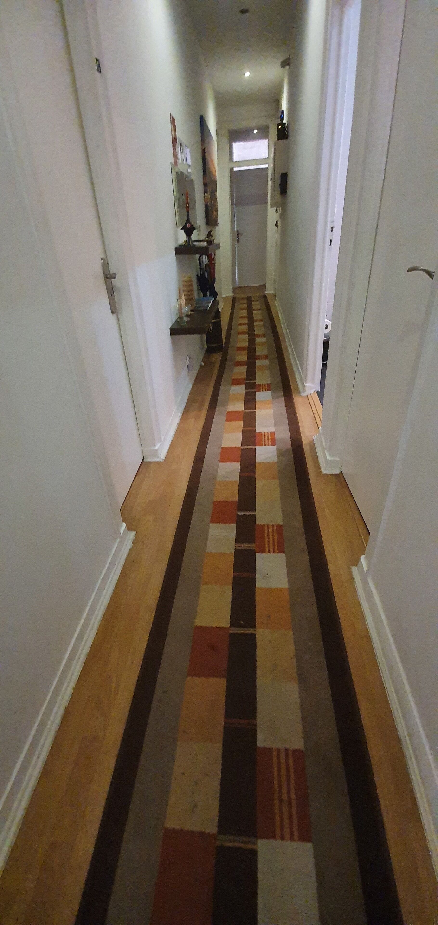 Un couloir avec un tapis à motifs, des murs blancs et une porte au fond.