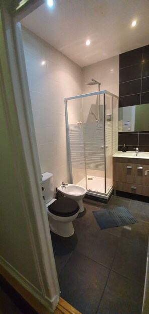 A modern bathroom with a glass-enclosed shower, a toilet, and a sink.