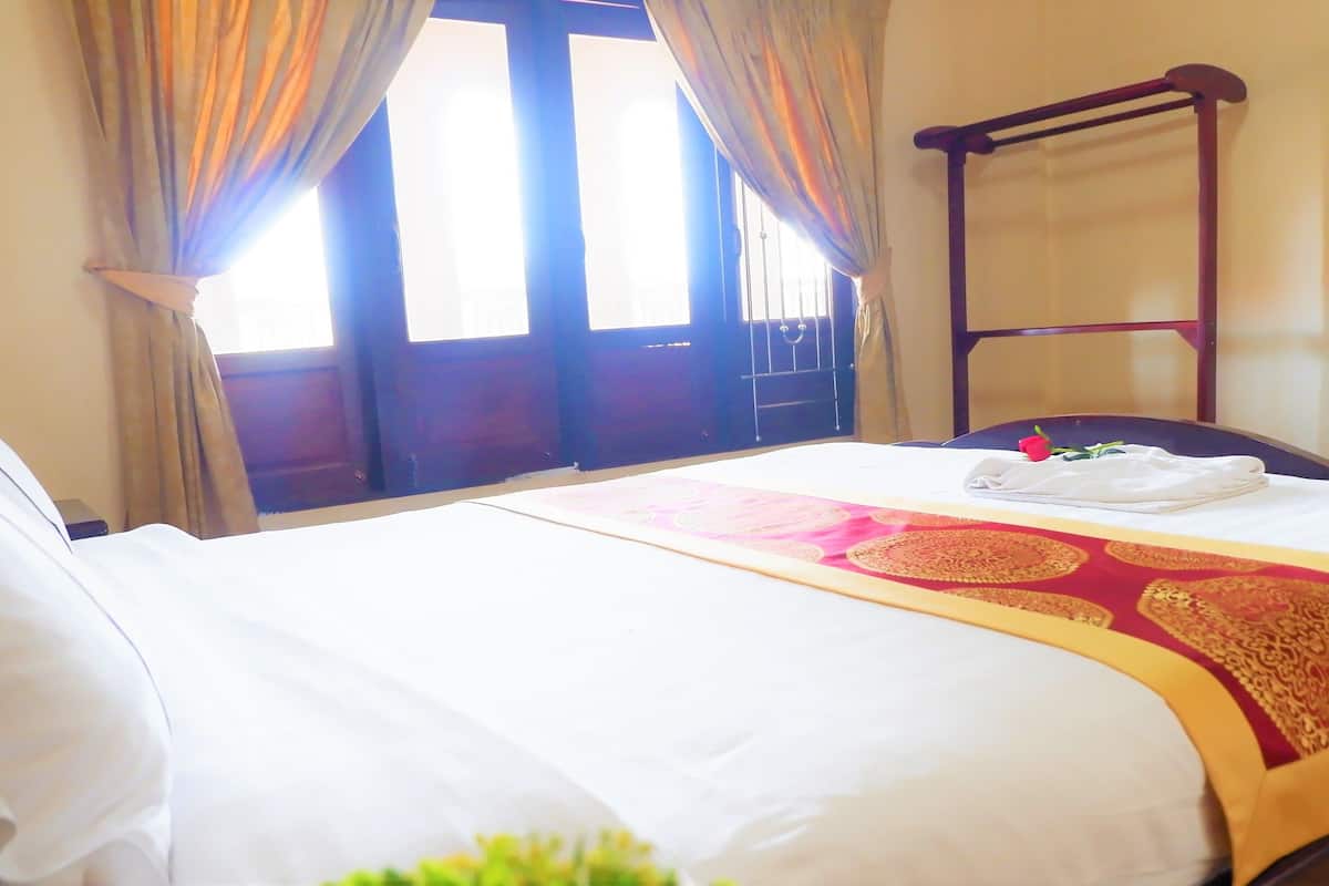 A hotel room with a bed, curtains, a wooden chair, and a window with curtains.