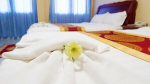 Habitación de hotel con una cama bien tendida, una colcha roja y dorada, y una flor blanca sobre la cama.