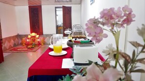Un comedor con una mesa roja, un vaso de jugo de naranja y una disposición tipo bufé.