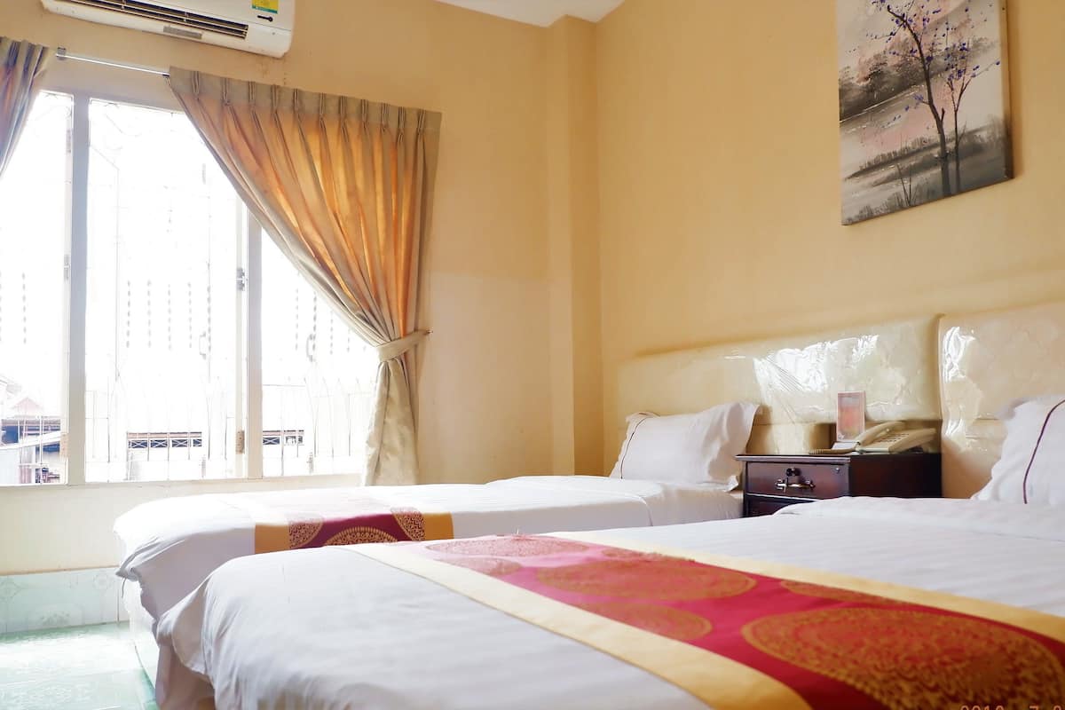 A hotel room with two beds, a nightstand with a phone and a lamp, a painting on the wall, and a window with curtains.