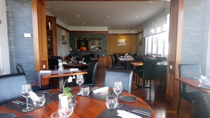 Un ristorante con tavoli rotondi apparecchiati per la cena, caratterizzato da sedie nere e tavoli in legno.