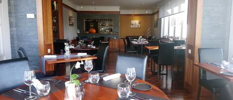 A restaurant with round tables set for dining, featuring black chairs and wooden tables.