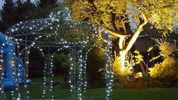 A gazebo with string lights, surrounded by a brick pathway and a grassy area.