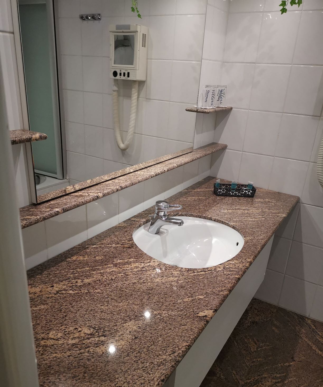 Een badkamer met een granieten aanrechtblad, een witte wastafel en een handspiegel.