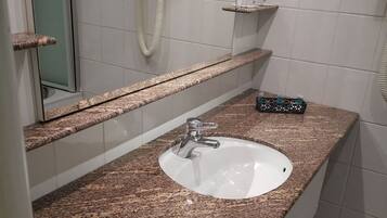 Een badkamer met een granieten aanrechtblad, een witte wastafel en een handspiegel.