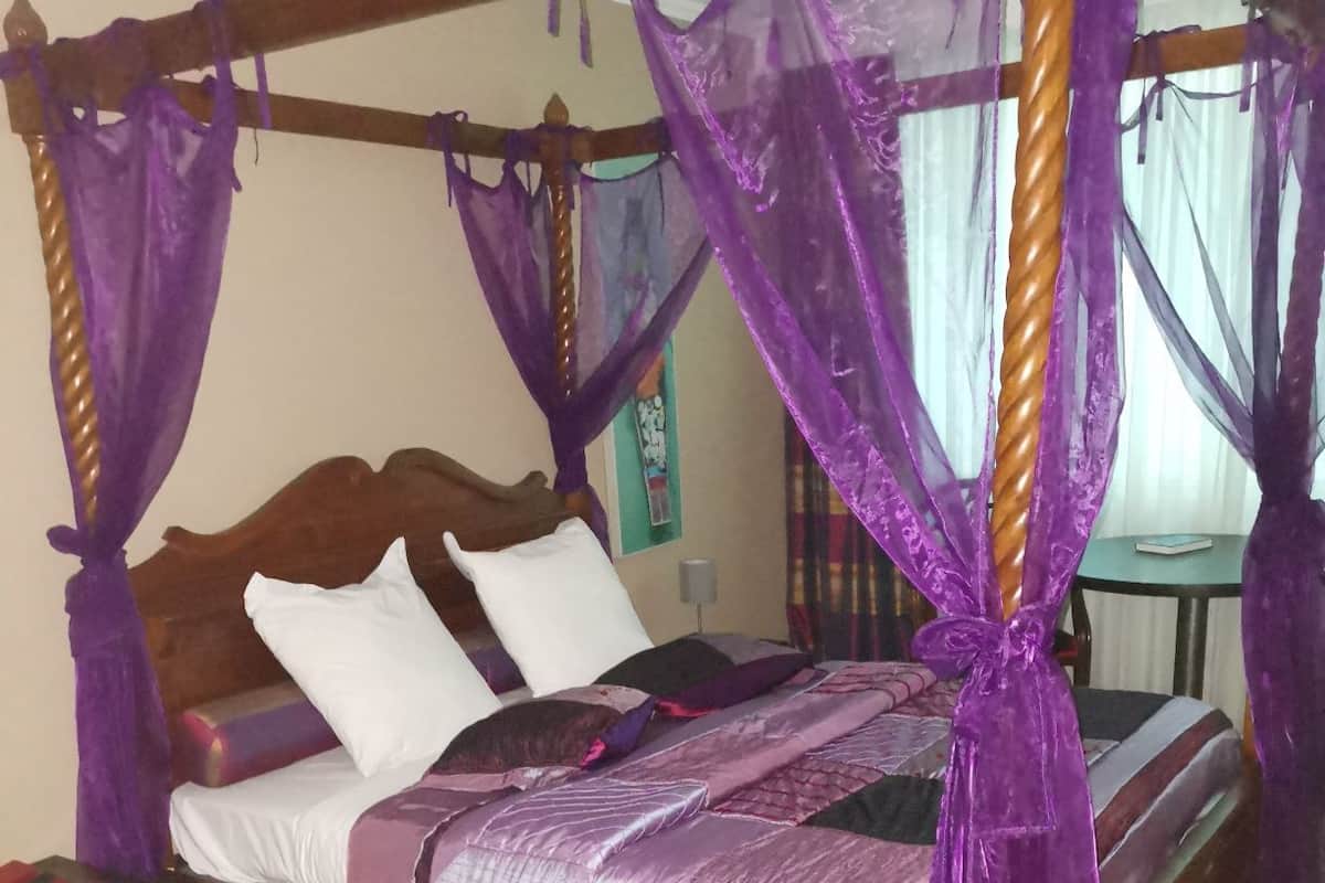 A four-poster bed with purple canopy, wooden headboard, white pillows, and a purple bedspread.