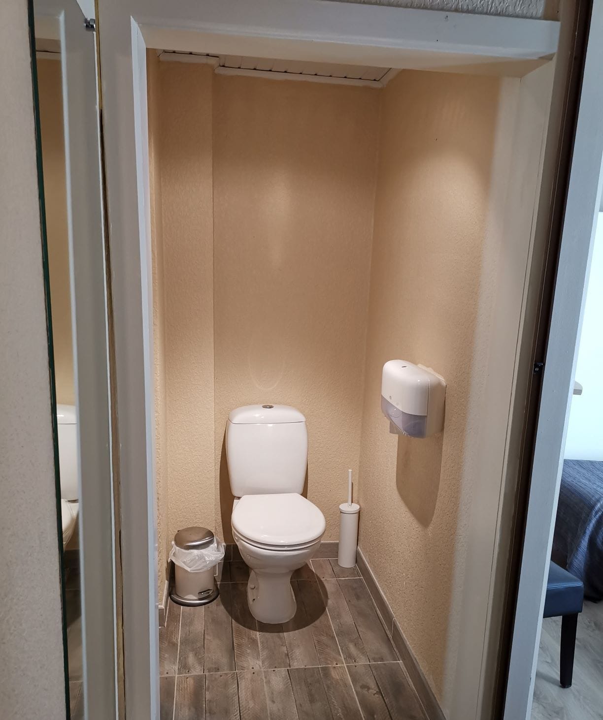 A small, compact bathroom with a toilet, a trash can, and a hand dryer.