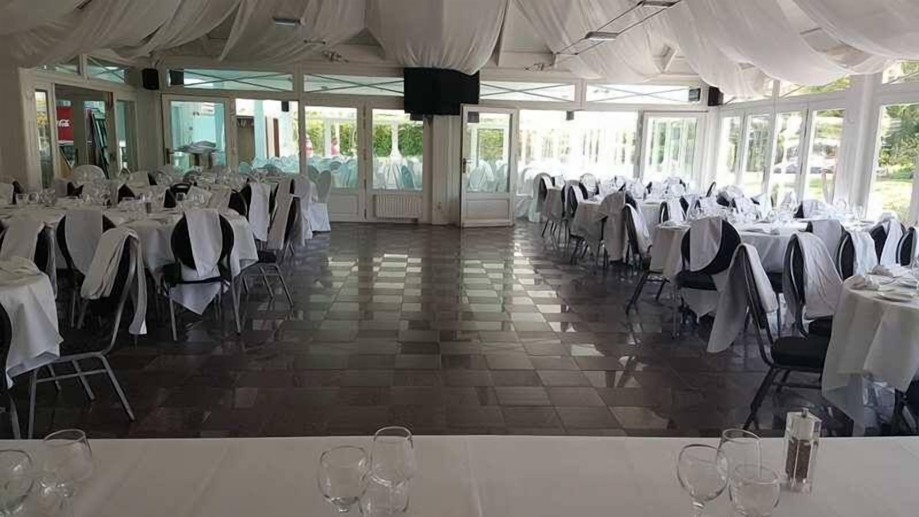 Un salón de banquetes con mesas dispuestas para un evento formal, con piso a cuadros y amplias ventanas.