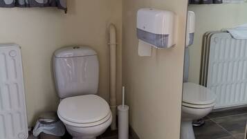 A bathroom with two toilets, a hand dryer, a trash bin, and a radiator.