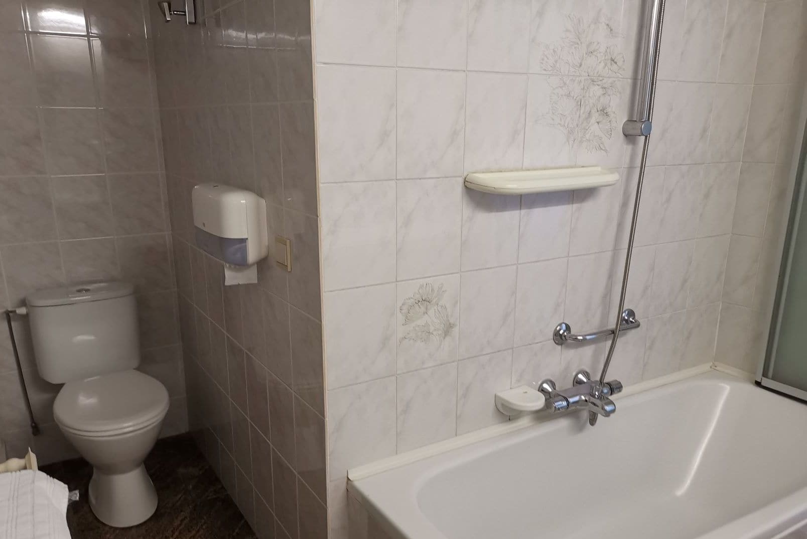 A bathroom with a toilet, a hand dryer, a shower with a glass door, and a bathtub.