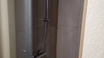 Una ducha moderna con múltiples cabezales y un rociador de mano, instalada en una pared con suelo de baldosas.