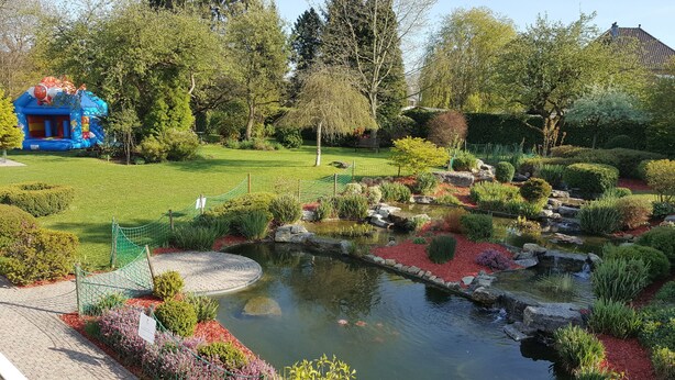 Un giardino con uno stagno, una struttura gonfiabile blu e diverse piante.