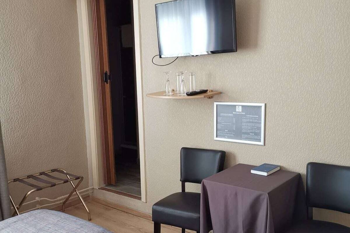 A hotel room with two beds, a TV, a small table with a chair, and a door leading to a balcony.
