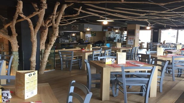 A restaurant with wooden tables and chairs, a menu stand, and a large tree branch decoration. - The Residence Galliate (Galliate)