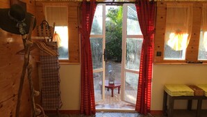 Una stanza in legno con un'ampia finestra, una sedia, un tavolo e un cappello appeso.
