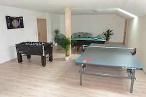 A room with a foosball table, a pool table, and a ping pong table.