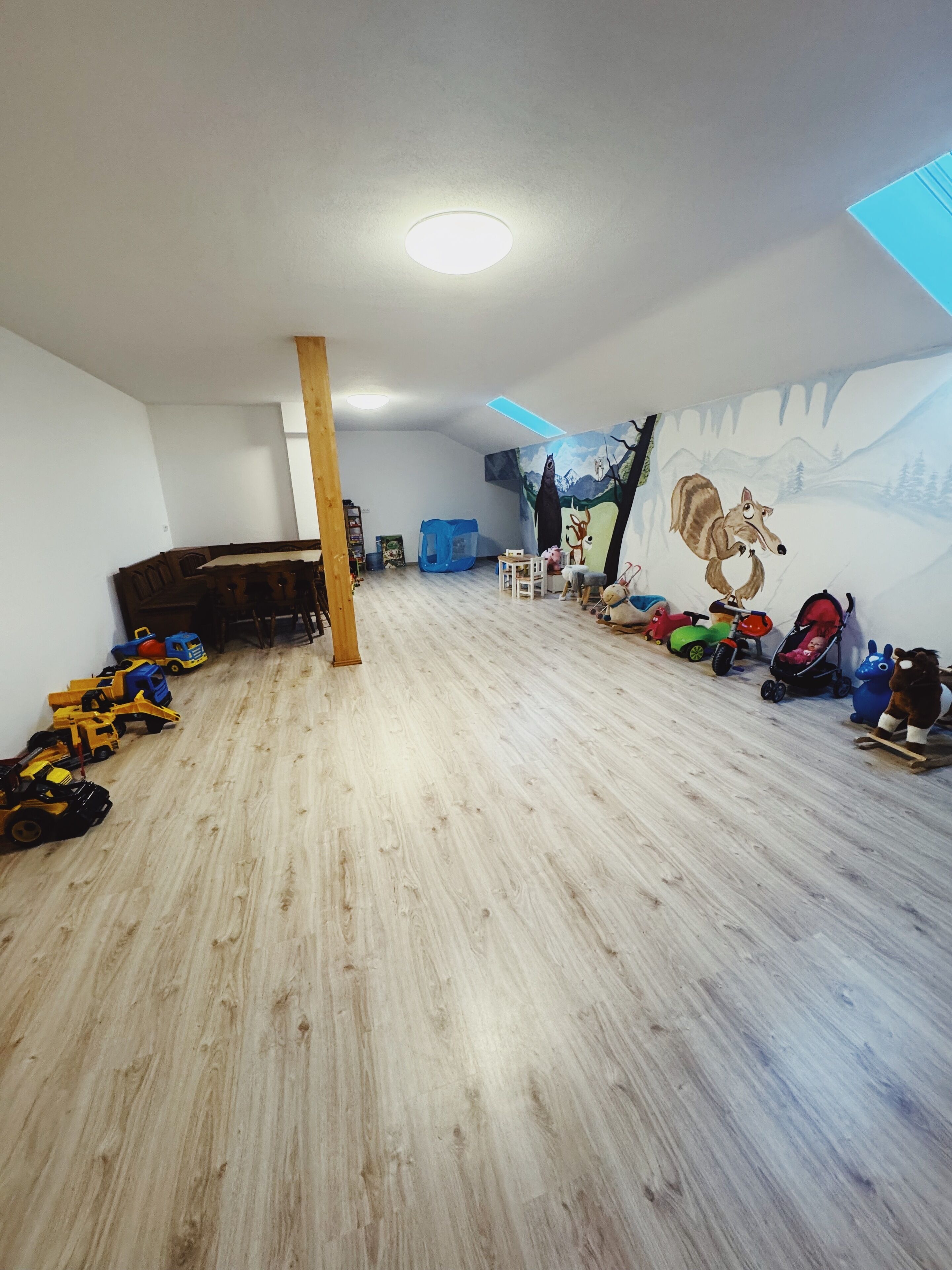 A child's playroom with a wooden floor, a mural on the wall, and various toys and play equipment.
