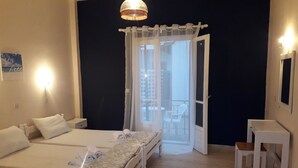 Ein Hotelzimmer mit zwei Betten, einem kleinen Tisch, einem Stuhl, einem Balkon mit Blick auf Gebäude und einer Hängelampe.