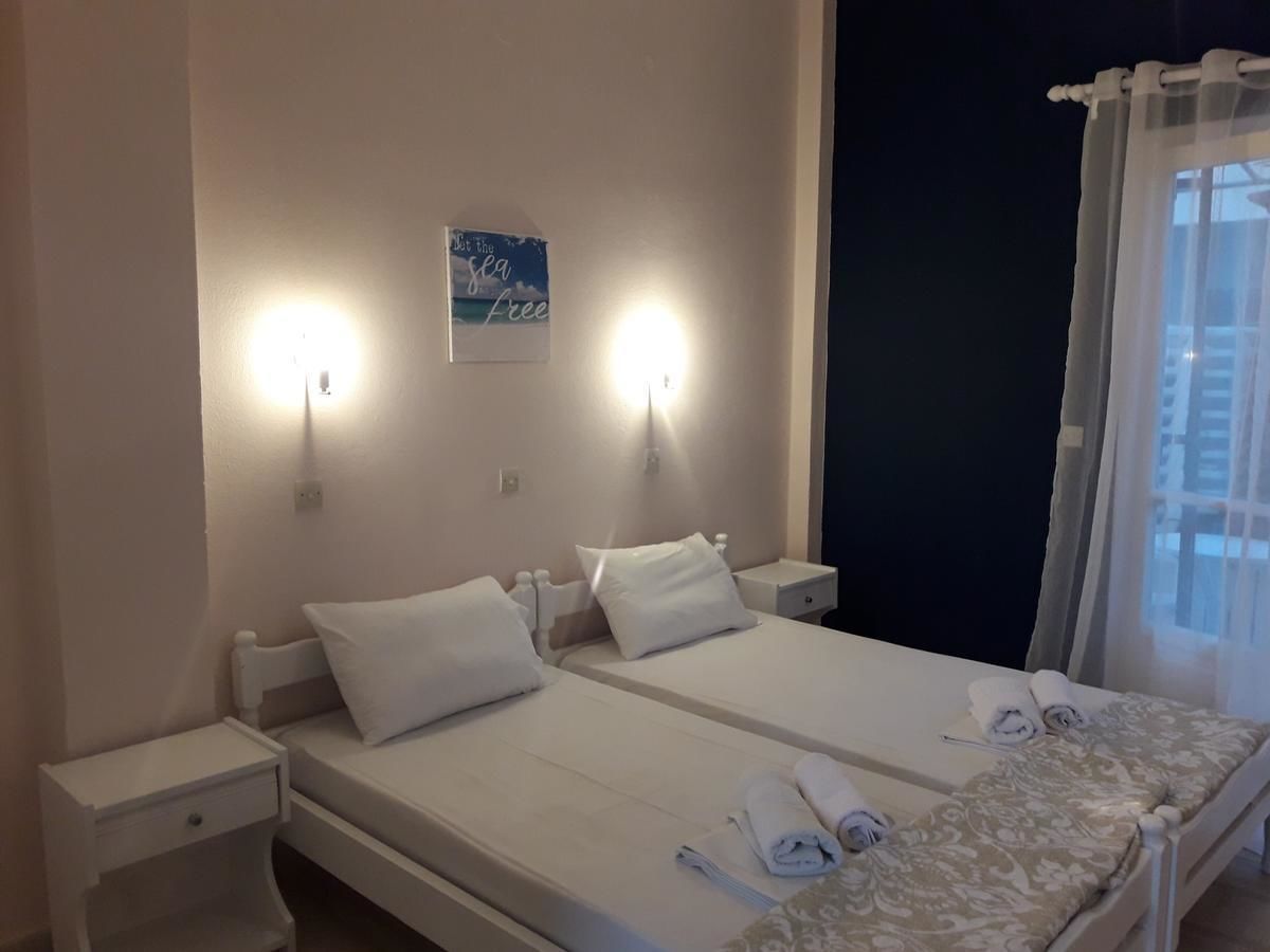 A hotel room with two beds, a nightstand, a wall-mounted light, and a window with curtains.