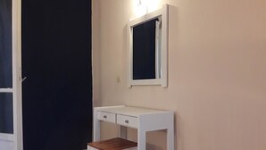Ein weißer Schreibtisch mit einem Spiegel darüber, platziert an einer Wand, links eine Tür.