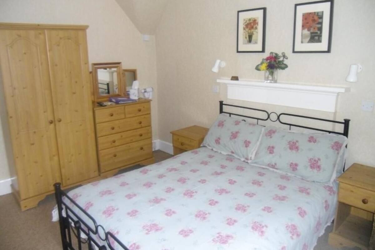 A bedroom with a bed, wooden wardrobe, bedside tables, and a mirror.