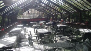 A covered outdoor dining area with tables and chairs, a greenhouse in the background, and hanging plants. - The Ormidale Hotel (Isle of Arran)