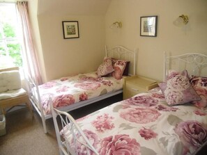 A bedroom with two single beds, each with floral bedding, a bedside table, and a chair. - The Ormidale Hotel (Isle of Arran)