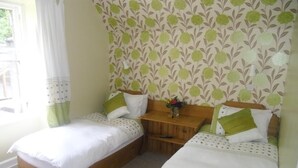 A bedroom with two single beds, a wooden nightstand, and a floral-patterned wallpaper. - The Ormidale Hotel (Isle of Arran)