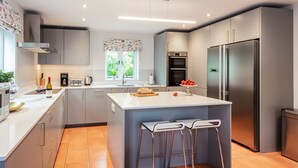 A modern kitchen with a central island, stainless steel appliances, and a window providing natural light. - Ship Bungalow (Minehead)