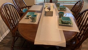 Mesa de comedor dispuesta con vajilla de diseño verde y blanco, rodeada de sillas de madera.