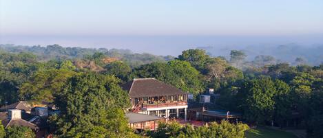 A large house with a spacious balcony, surrounded by dense forest.
