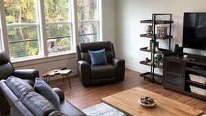 A modern living room with a leather sofa, a recliner, a coffee table, and a TV stand with shelves. - CHARMING AND SPECTACULAR RIVERFRONT HOUSE, BEAUTIFUL IN ANY SEASON OF THE YEAR! (Leaburg)