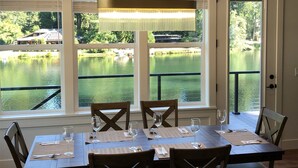 A dining area with a table set for six, large windows with a view of a lake, and a chandelier above. - CHARMING AND SPECTACULAR RIVERFRONT HOUSE, BEAUTIFUL IN ANY SEASON OF THE YEAR! (Leaburg)