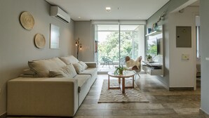 A modern living room with a beige sofa, a coffee table, and a glass door leading to an outdoor area. - OXO Bertoni Luxury BBQ & Pool (Asunción)