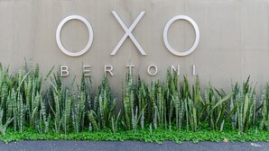 A sign with the name "OXO BERTONI" on a beige wall, surrounded by green plants. - OXO Bertoni Luxury BBQ & Pool (Asunción)