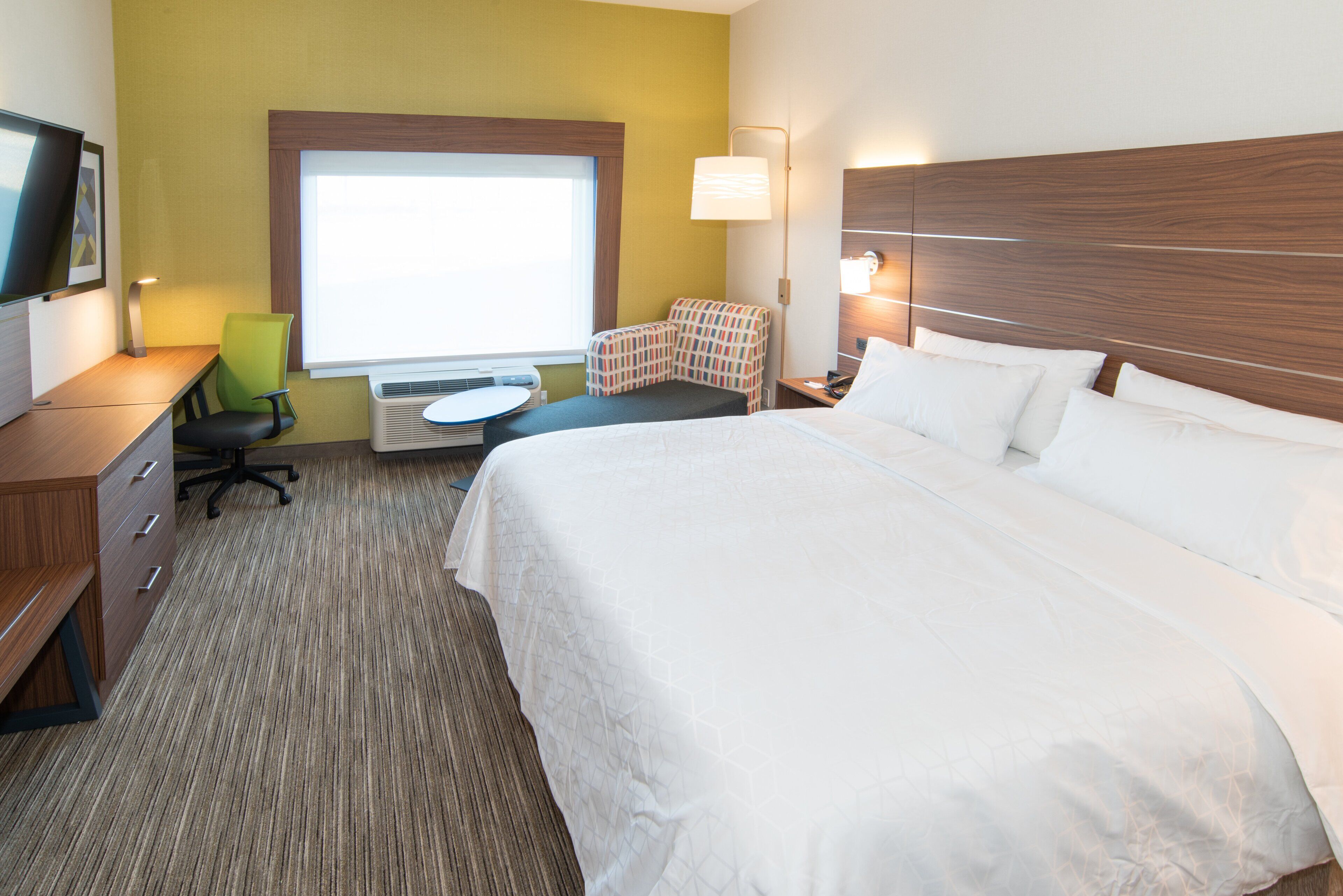 A hotel room with a large bed, a desk with a chair, a small table, and a window.