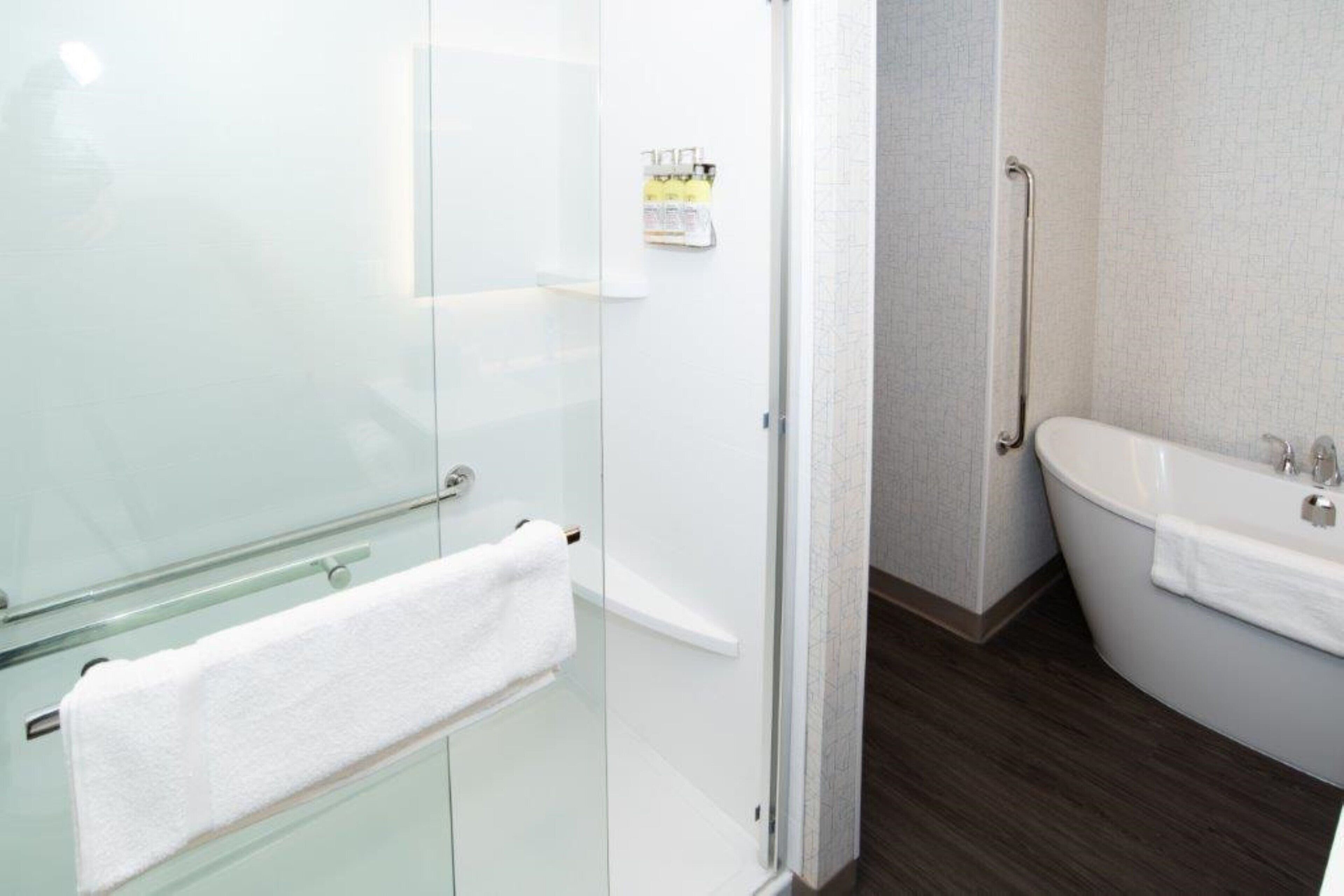 A modern bathroom with a glass shower enclosure, a white bathtub, and a wooden floor.