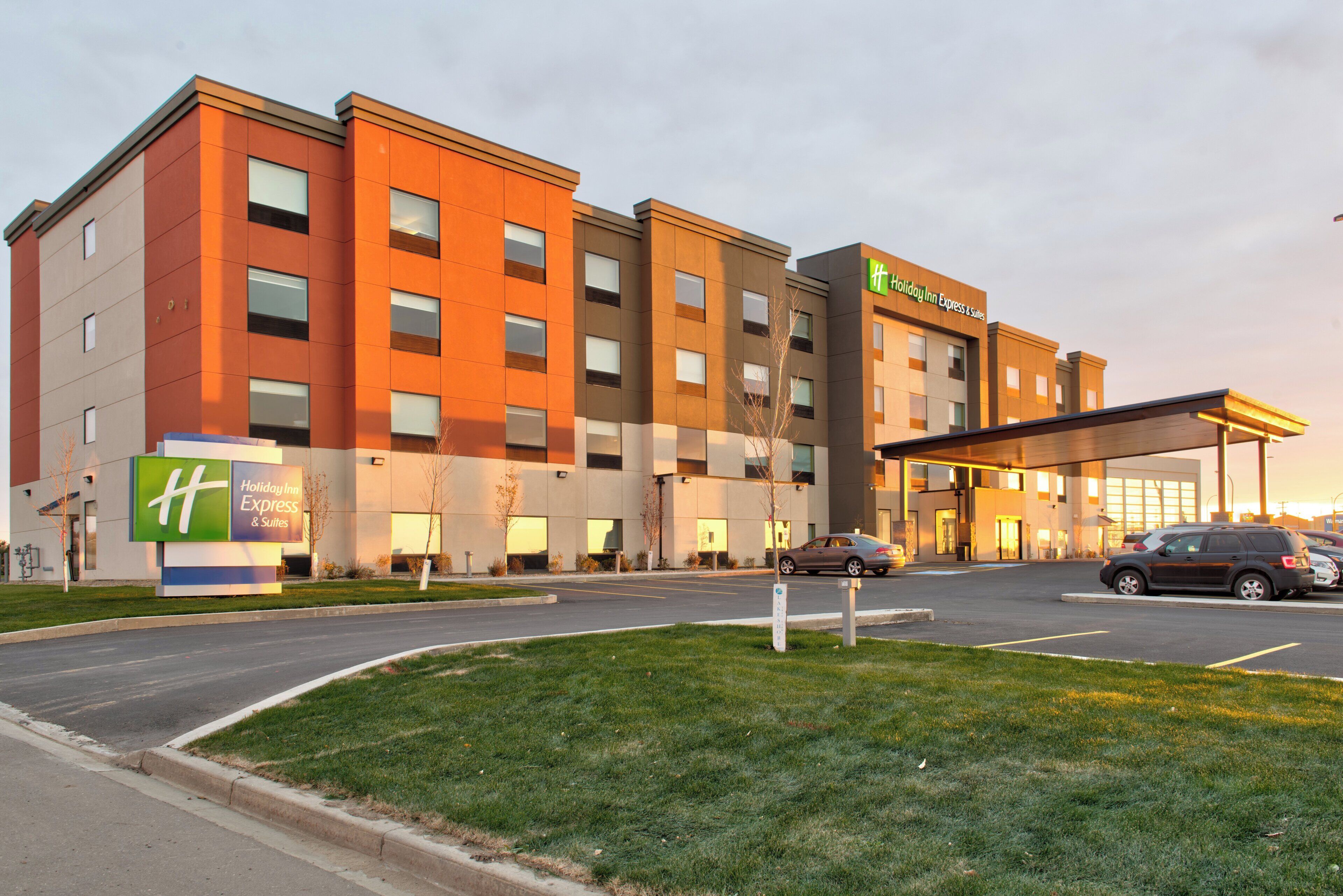 Edificio de Holiday Inn Express & Suites con diseño moderno, que cuenta con un amplio estacionamiento y un cielo despejado.