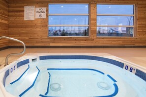 Un bain à remous avec un intérieur en bois, une fenêtre donnant sur un bâtiment et un panneau indiquant les règles à respecter au bord de la piscine.