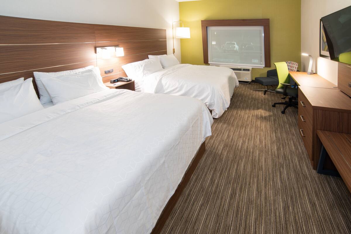 A hotel room with two beds, a desk, a chair, a TV, and a large window.