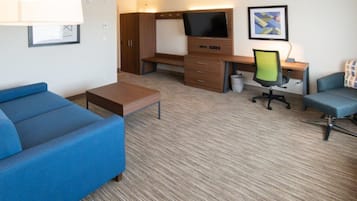 Habitación de hotel con un sofá azul, un escritorio de madera con un televisor, una silla y una pequeña mesa.