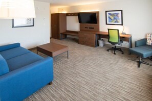 Ein Hotelzimmer mit einem blauen Sofa, einem Holztisch mit Fernseher, einem Stuhl und einem kleinen Tisch.