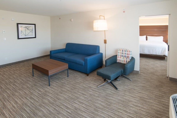 Habitación de hotel con sofá azul, una mesa de madera, un sillón estampado y una cama con ropa blanca.