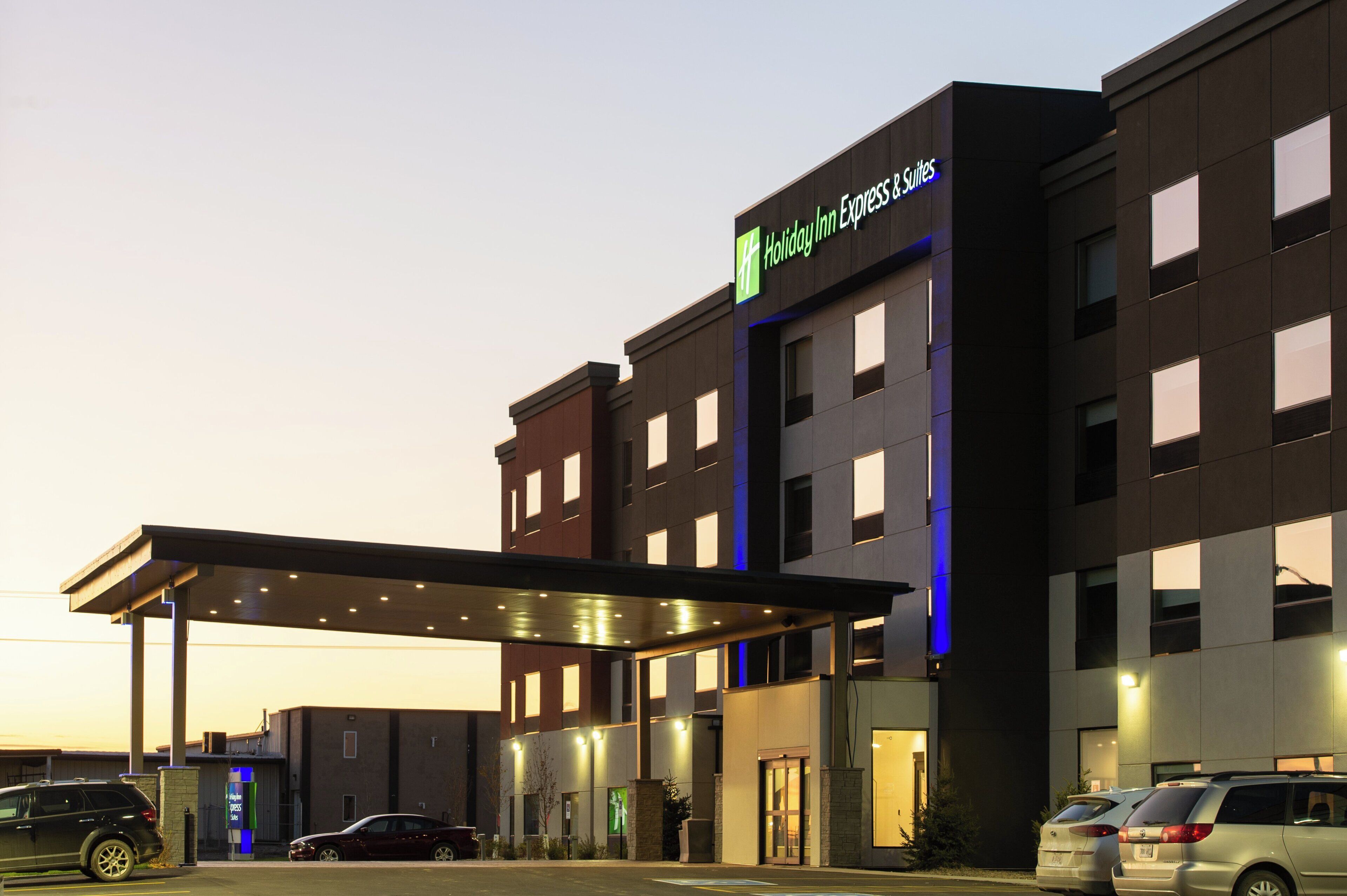 Edificio de Holiday Inn Express & Suites con entrada cubierta, varias ventanas y un estacionamiento con automóviles.