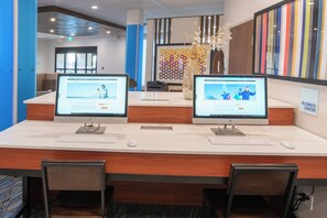 A reception desk with two HP monitors displaying the IHG Rewards Club website, a business center sign, and a decorative vase with branches.