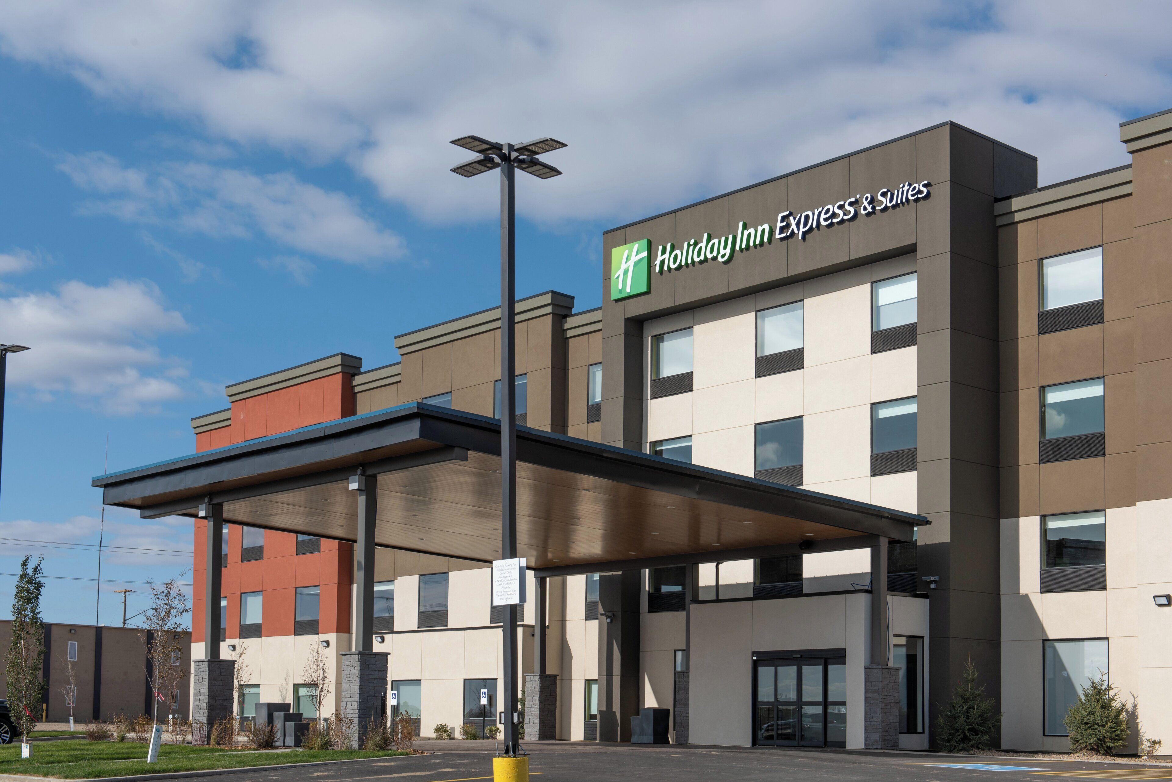 A Holiday Inn Express & Suites building with a covered entrance, clear sky, and a parking lot.